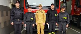 Zdjęcie przedstawia 5 strażaków: komendanta, dowódcę JRG oraz trzech awansowanych strażaków. Stoją oni w szeregu pozując do zdjęcia na tle samochodu ratowniczo-gaśniczego znajdującego się w garażu komendy.