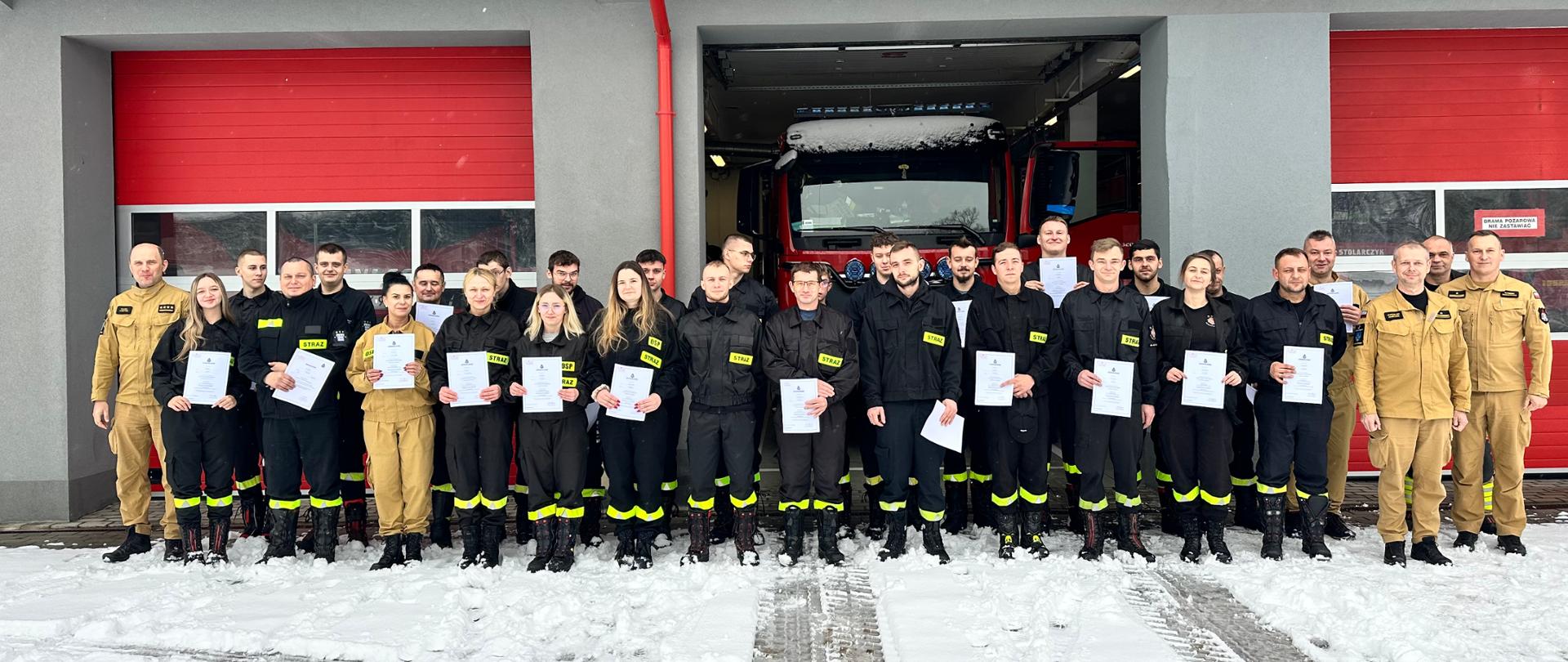 Strażacy stojący z dyplomami przed budynkiem 