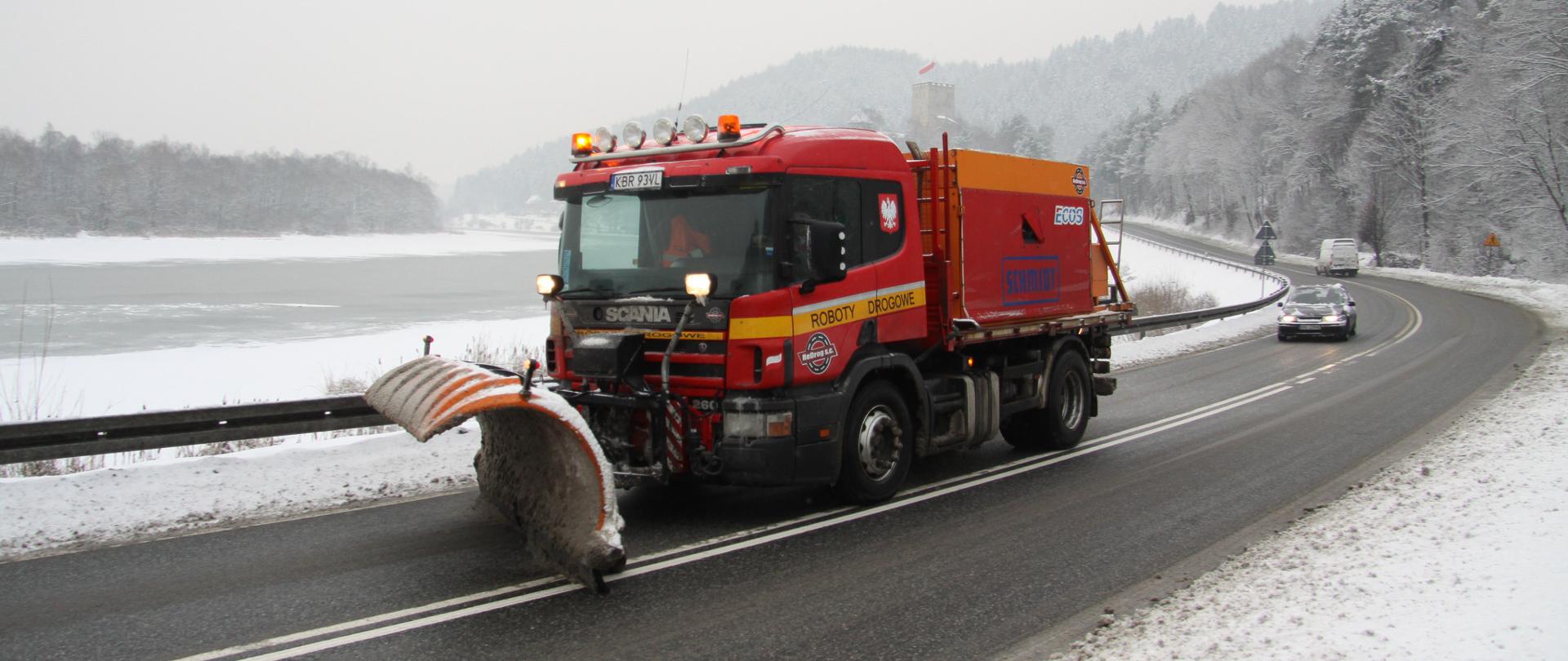 Zimowe utrzymanie DK75, okolice zamku Tropsztyn w woj. małopolskie. Na pierwszym planie pługosolarka pracująca na drodze i zimowy krajobraz.