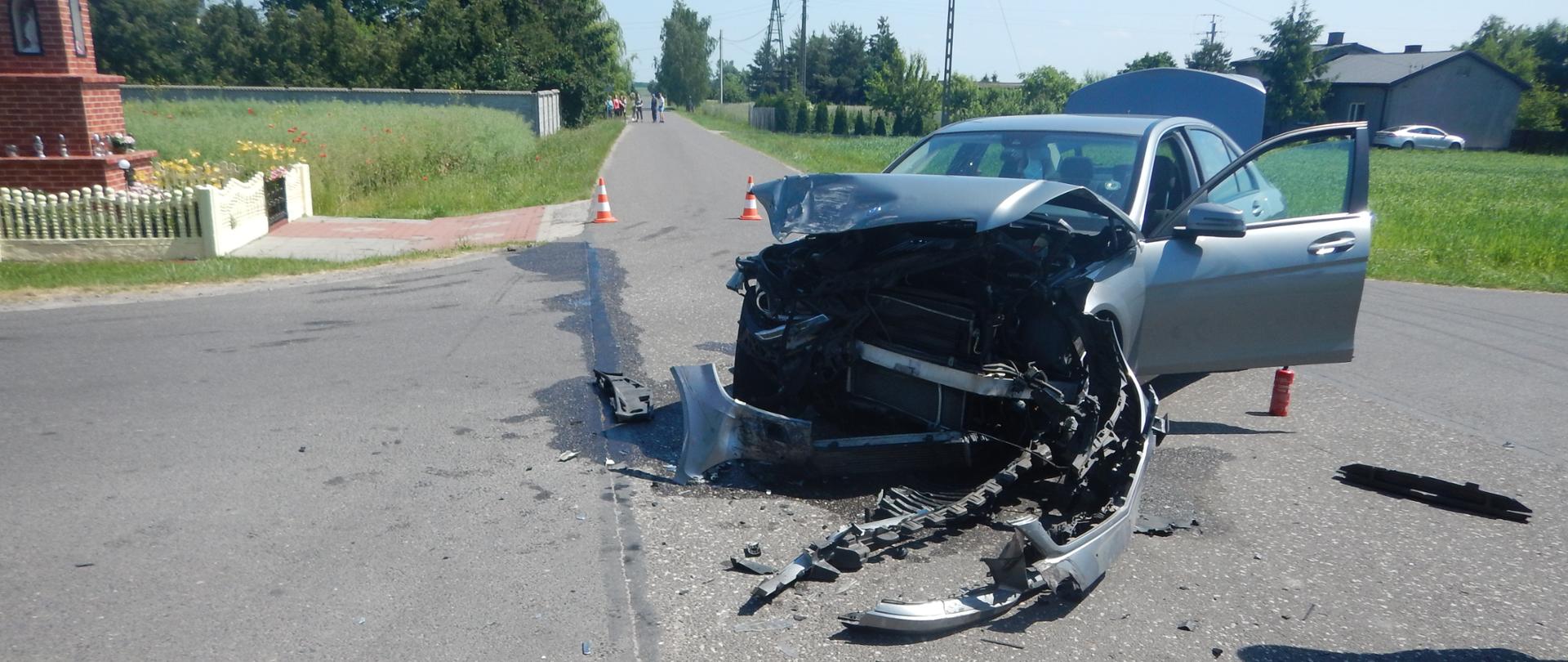 Zdjęcie przedstawia srebrny samochód osobowy, który brał udział w wypadku drogowym. Samochód ma uszkodzony przód.