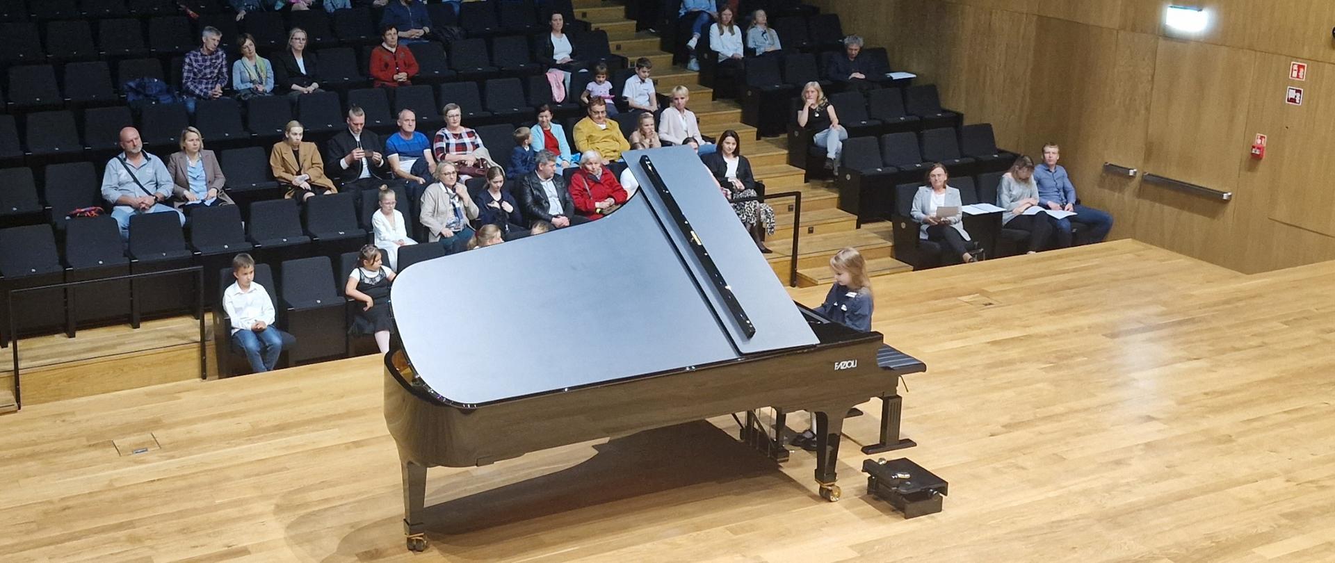 Dziewczynka gra na fortepianie Fazioli, w tle widać publiczność na widowni.