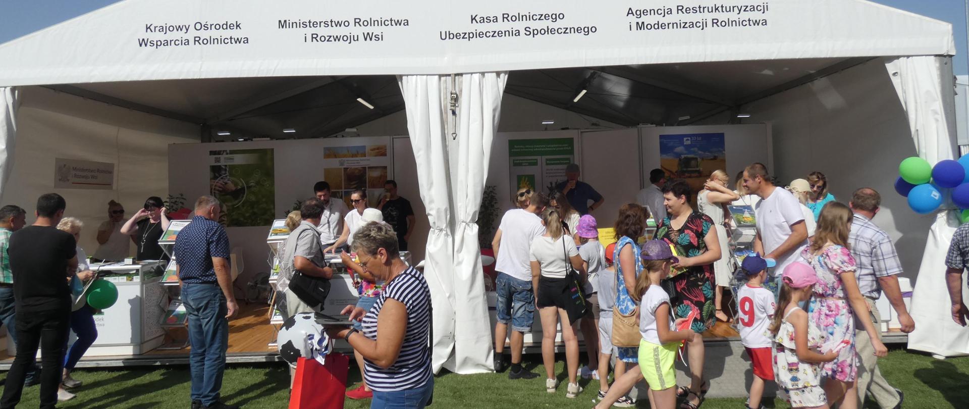 Duża grupa odwiedzających stoisko informacyjne MRiRW, KRUS, ARiMR i KOWR pod namiotem.