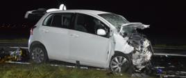 Wypadek na drodze wojewódzkiej nr 309. Zderzenie trzech pojazdów. Na pierwszym planie wrak toyoty, która ma bardzo mocno uszkodzony przód, w tym przednią szybę. Auto jest koloru białego. Za autem na jezdni leży koc termiczny, przed - porozrzucane elementy samochodów.