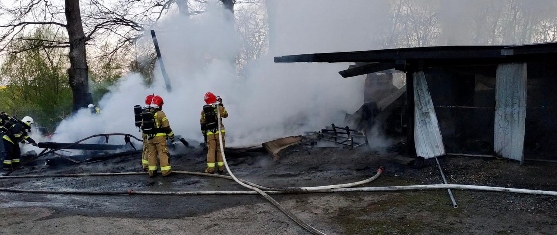 strażacy na tle dymu z pożaru garażu, widoczne linie wężowe