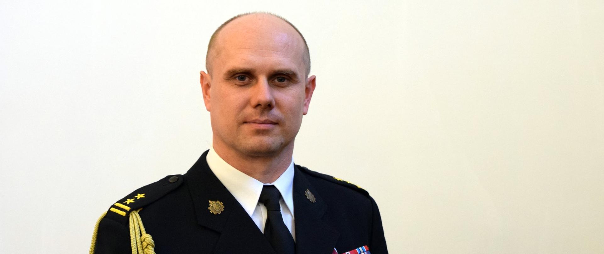 Zdjęcie portretowe komendanta bryg. Łukasza Kapinosa na jasnym tle w mundurze galowym