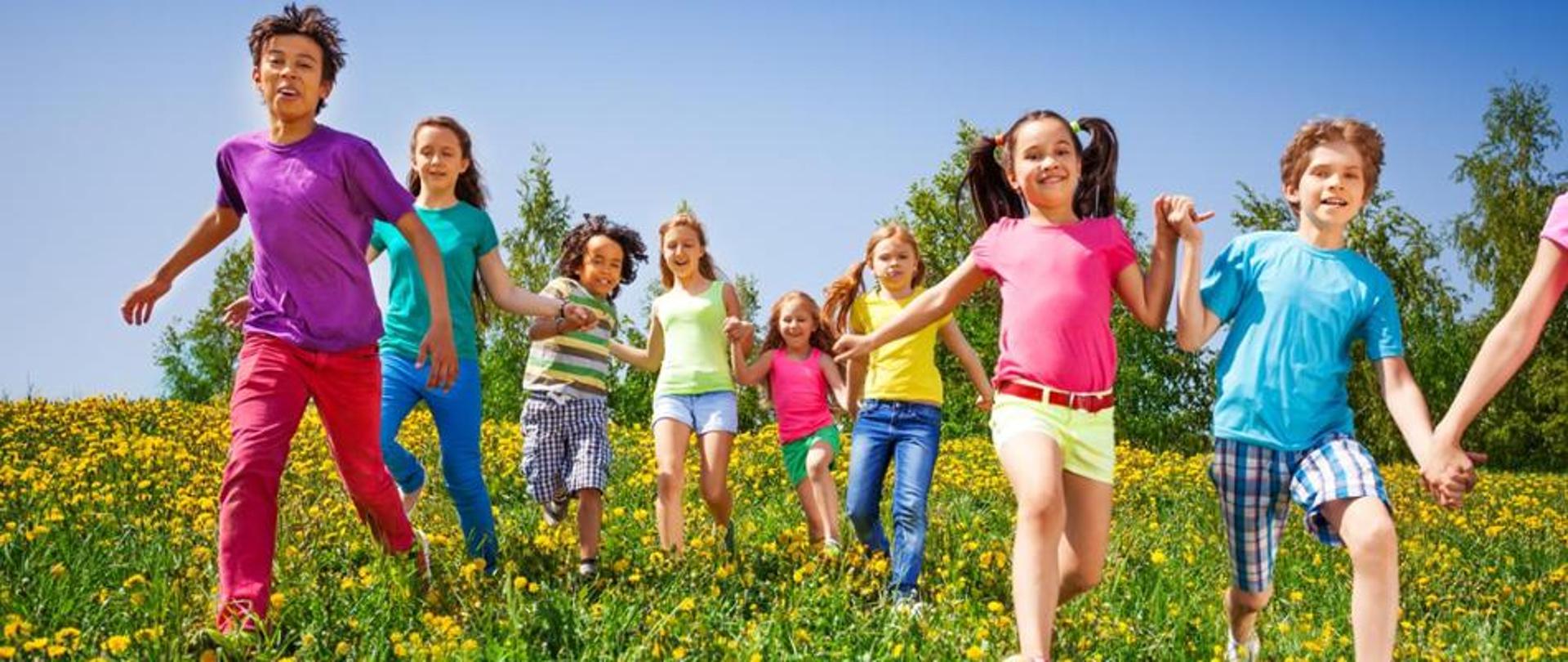 łąka po której biegną dzieci dziewczynki i chłopcy w kolorowych letnich strojach