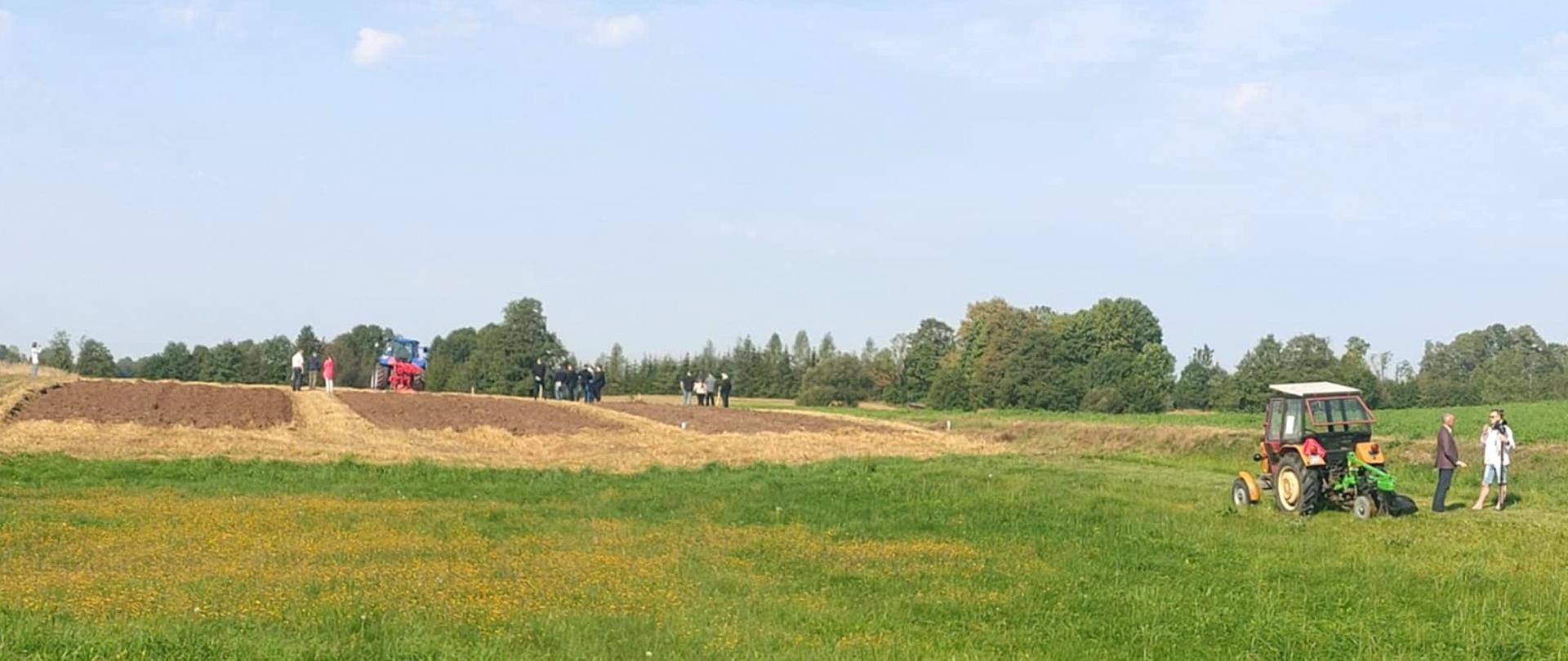 Traktor podczas orki, rozproszone grupki ludzi