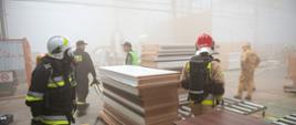 Strażacy przy działaniach w zadymionej hali przemysłowej.