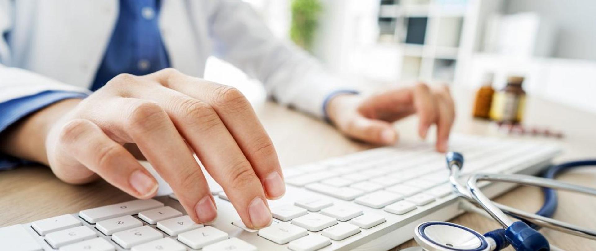 na zdjęciu widać dłonie klawiaturę i stetoskop 