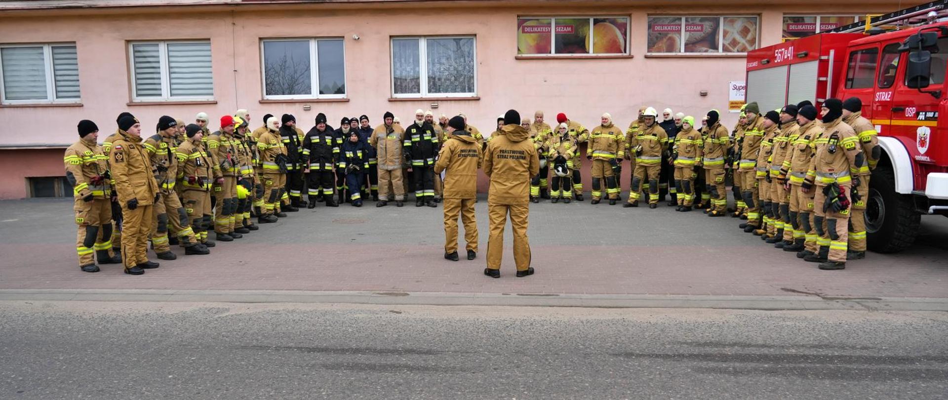 grupa strażaków w mundurach na zbiórce ustawieni w kształcie litery C