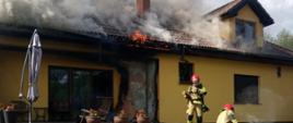 Zdjęcie przedstawia strażaków gaszących pożar domu w miejscowości Chodzież.
W tle budynki.
