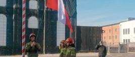 Strażacy na placu komendy wciągają flagę państwową na maszt i salutują