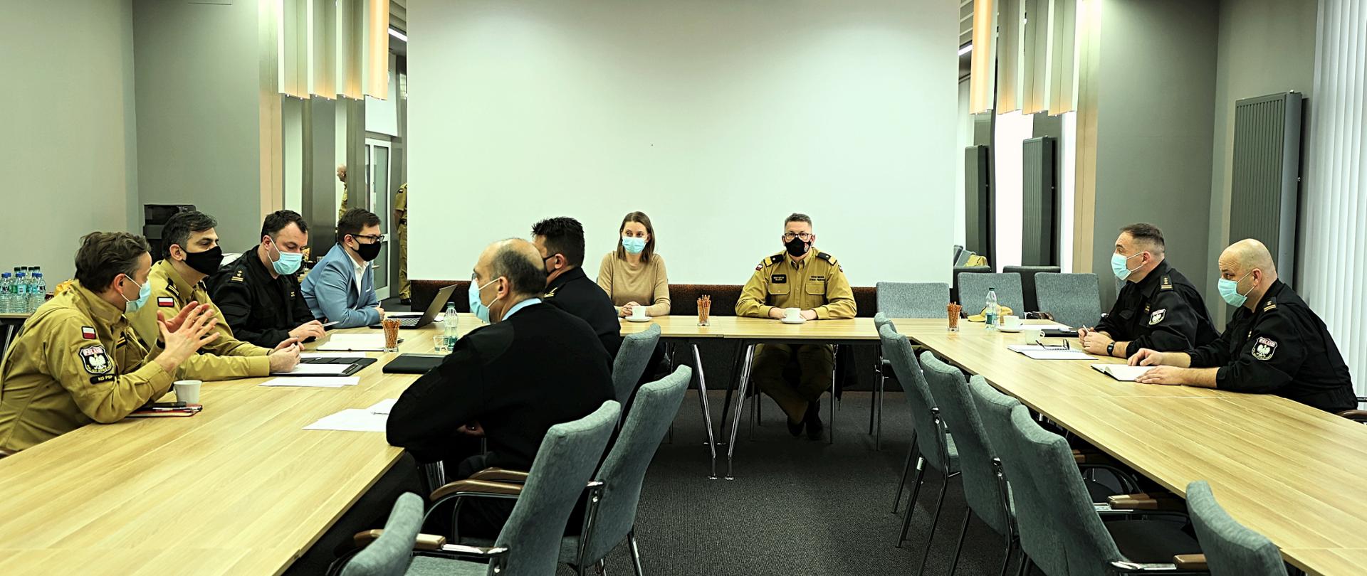 Sala konferencyjna z uczestnikami spotkania siedzącymi za stołem. W spotkani uczestniczą: Pani Krystyna Sikorska z Biura Strategii i Transformacji Rządowej Agencji Rezerw Strategicznych, nadbrygadier Krzysztof Hejduk zastępca komendanta głównego PSP, dyrektorzy biur KG PSP oraz kanclerz SGSP.