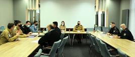 Sala konferencyjna z uczestnikami spotkania siedzącymi za stołem. W spotkani uczestniczą: Pani Krystyna Sikorska z Biura Strategii i Transformacji Rządowej Agencji Rezerw Strategicznych, nadbrygadier Krzysztof Hejduk zastępca komendanta głównego PSP, dyrektorzy biur KG PSP oraz kanclerz SGSP.