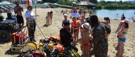 Na zdjęciu strażacy i policjanci oraz dzieci podczas pogadanki na plaży