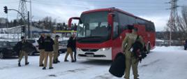 Strażacy w mundurach z napisem USAR Poland pakują torby do autobusu przed pojazdem stoi kierownictwo Komendy Wojewódzkiej Państwowej Straży Pożarnej w Gdańsku.