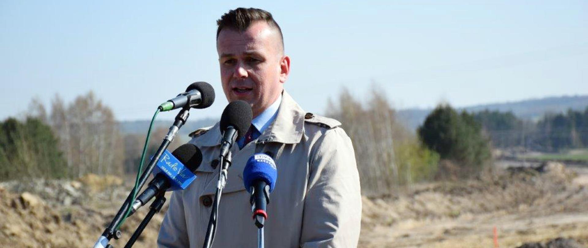 Na tle budowy wiceminister Adam Hamryszczak przemawia do mikrofonów