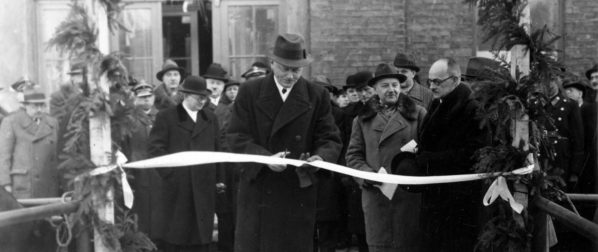 Na zdjęciu Michał Gnoiński wojewoda krakowski przecina wstęgę. Wstęga zawieszona jest między dwoma przystrojonymi świerkiem. Za wojewodą stoi kilkadziesiąt osób, które przygląda się wydarzeniu.