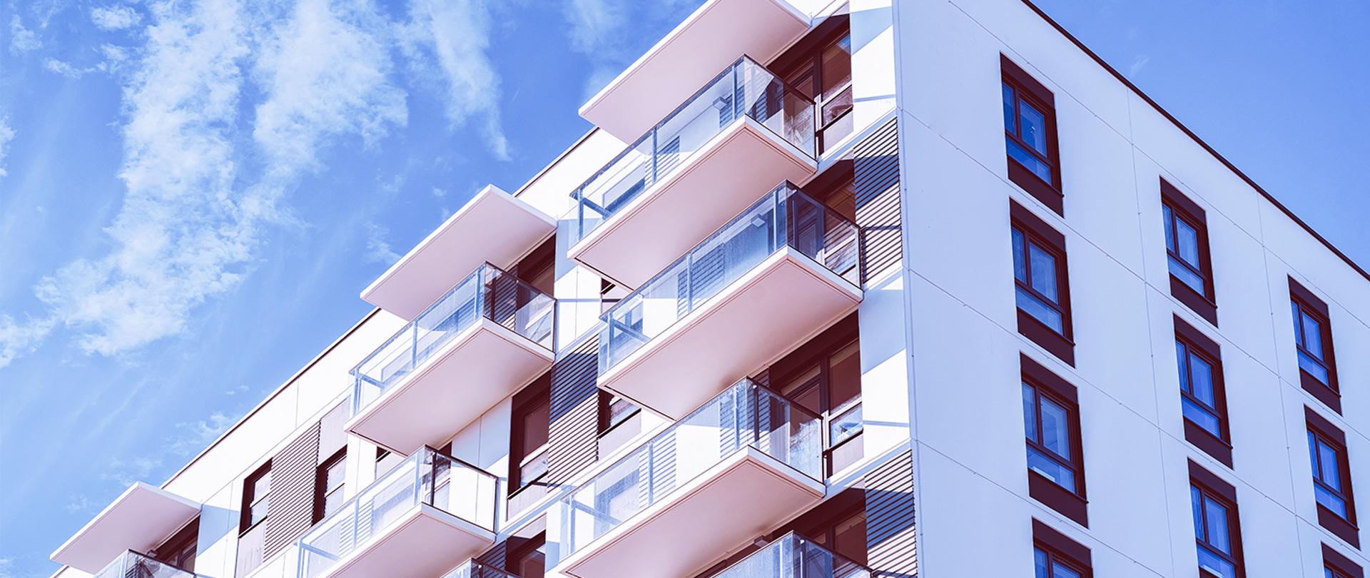 Na zdjęciu fragment bloku mieszkalnego na tle słonecznego nieba.