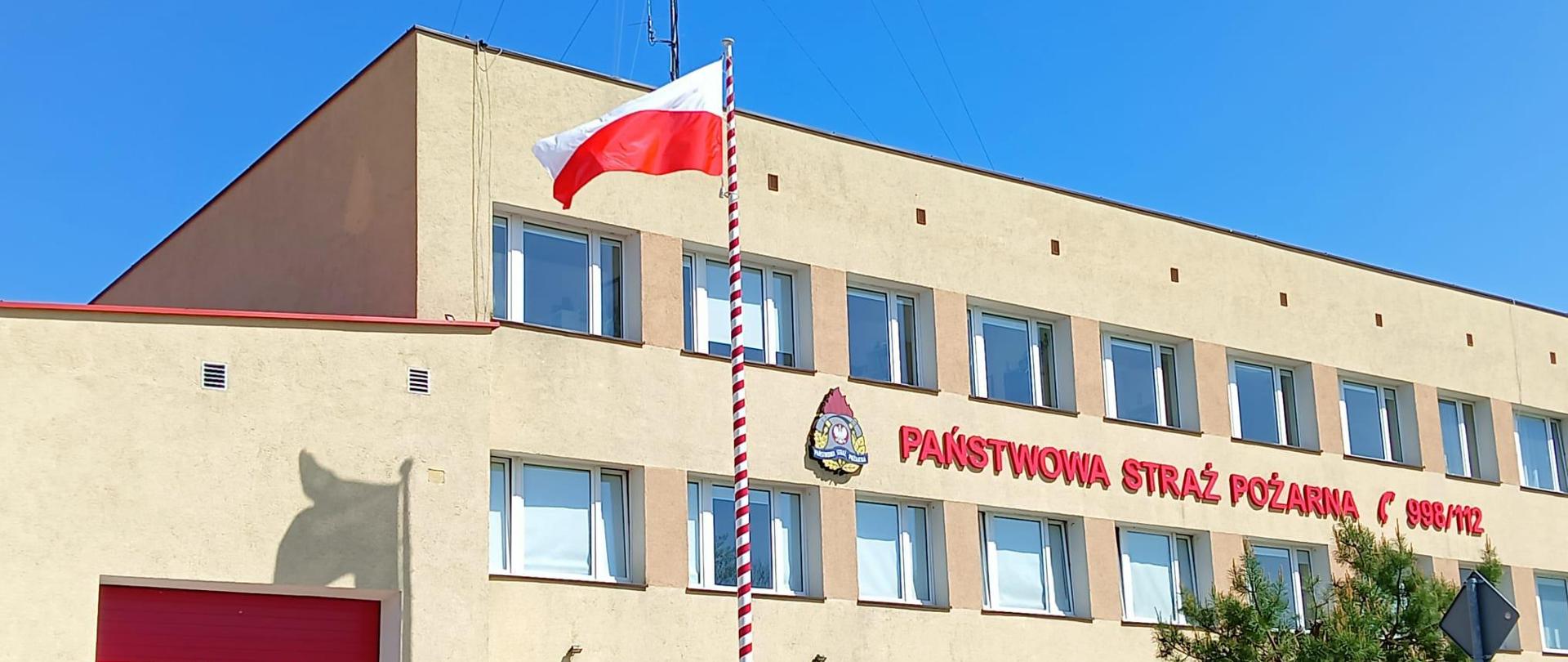 Na zdjęciu widać budynek Komendy Powiatowej Państwowej Straży Pożarnej. Przed budynkiem na maszcie powiewa Flaga.