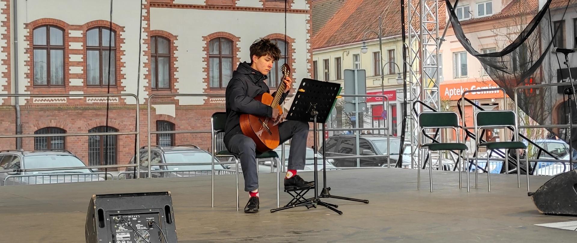 Na zbudowanej scenie z centrum miasta Pisza uczeń gra na gitarze.