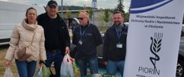 Grupa osób przy plenerowym stoisku informacyjnym stojących obok baneru i stolika z ulotkami.