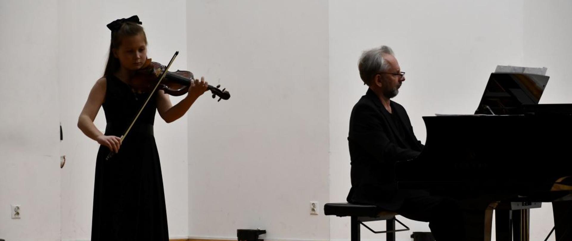 Zdjęcie kolorowe. Na scenie stoi Milena Kukulska w długiej czarnej sukience ze skrzypcami, a obok przy fortepianie siedzi akompaniator Tomasz Szymczewski.