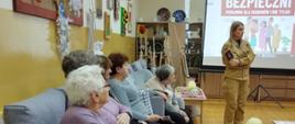 Strażak prowadzące prelekcję, na pierwszym planie słuchacze, w tle wyświetlana prezentacja 