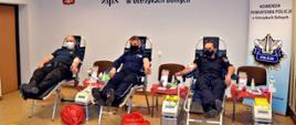 Na zdjęciu zastępca komendanta powiatowego PSP w Ustrzykach Dolnych wraz z komendantami policji, oddają krew. W tle logo Komendy Powiatowej Policji.