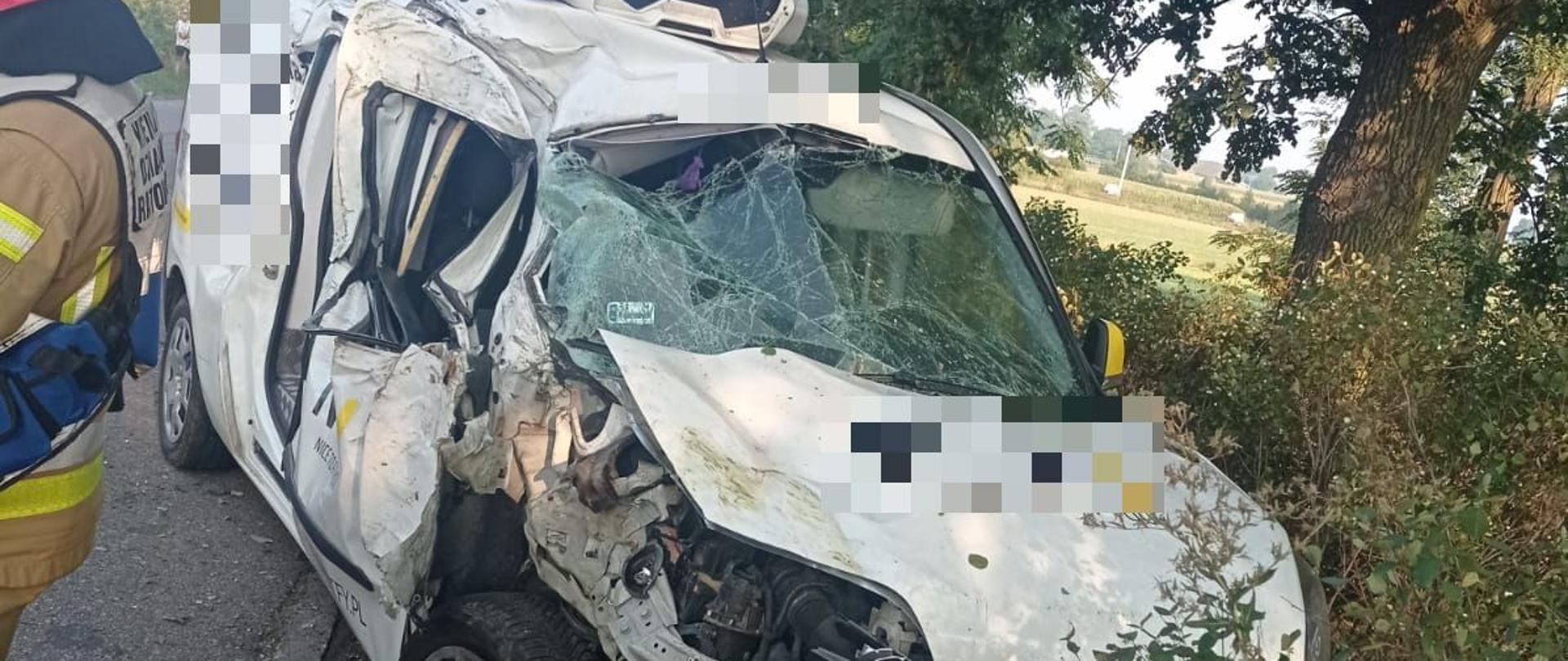 uszkodzony samochód osobowy stoi na poboczy drogi obok strażak 