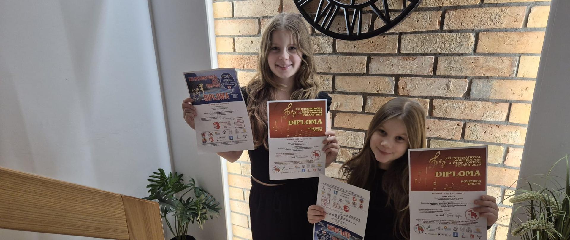 Uczennice ZPSM stoją na tle ceglanej ściany i trzymają dyplomy w rękach