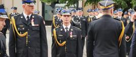 Zdjęcie przedstawia nagrodzonych medalem stających po wręczenie medalu. w tle zgromadzeni strażacy.