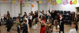 Bal karnawałowy. Grupa dzieci tańczy w sali przystrojonej kolorowymi balonami.