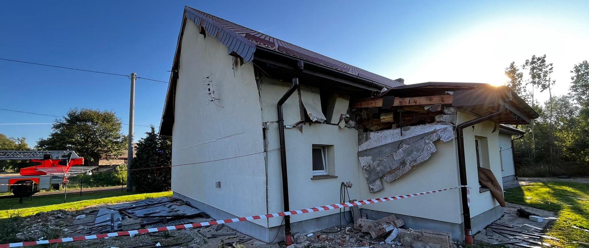Zdjęcie przedstawia zniszczony dom jednorodzinny po wybuchu gazu wewnątrz obiektu. W tle widoczna drabina mechaniczna.