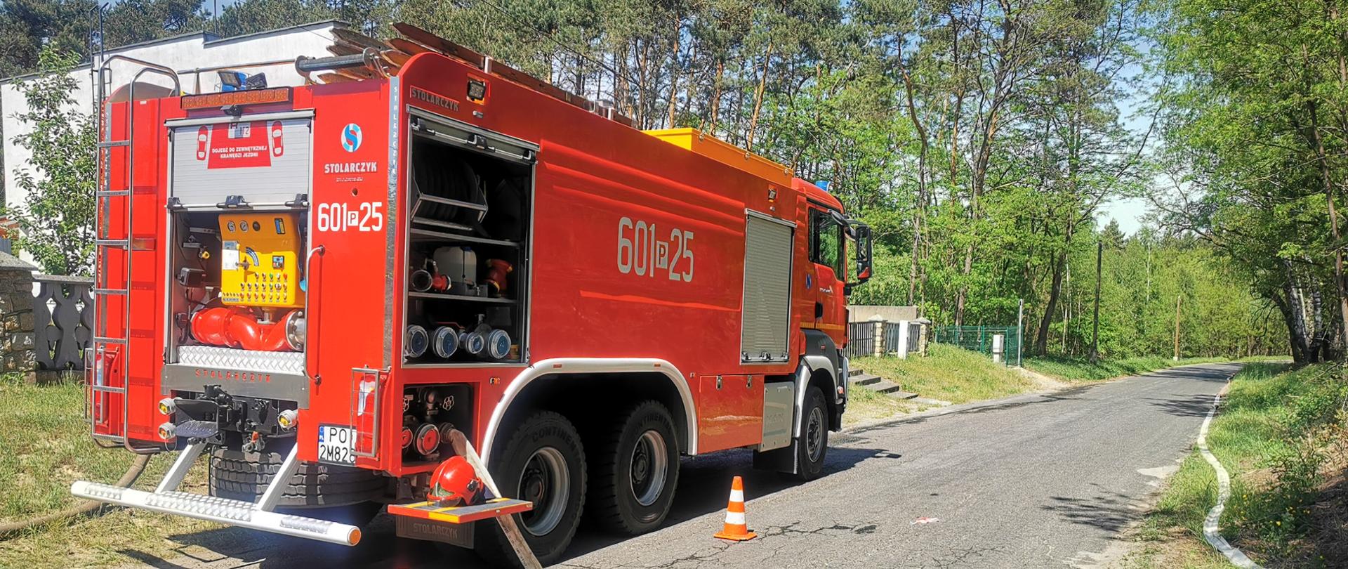 Na zdjęciu samochód ratowniczo gaśniczy przy drodze na jezdni rozwinięty wąż zabezpieczony mostkami przejazdowymi, obok pachołek Linia puszczona poboczem drogi