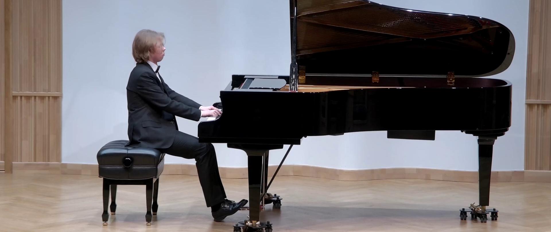 Zdjęcie. Na estradzie sali koncertowej pianista gra na dużym czarnym fortepianie.