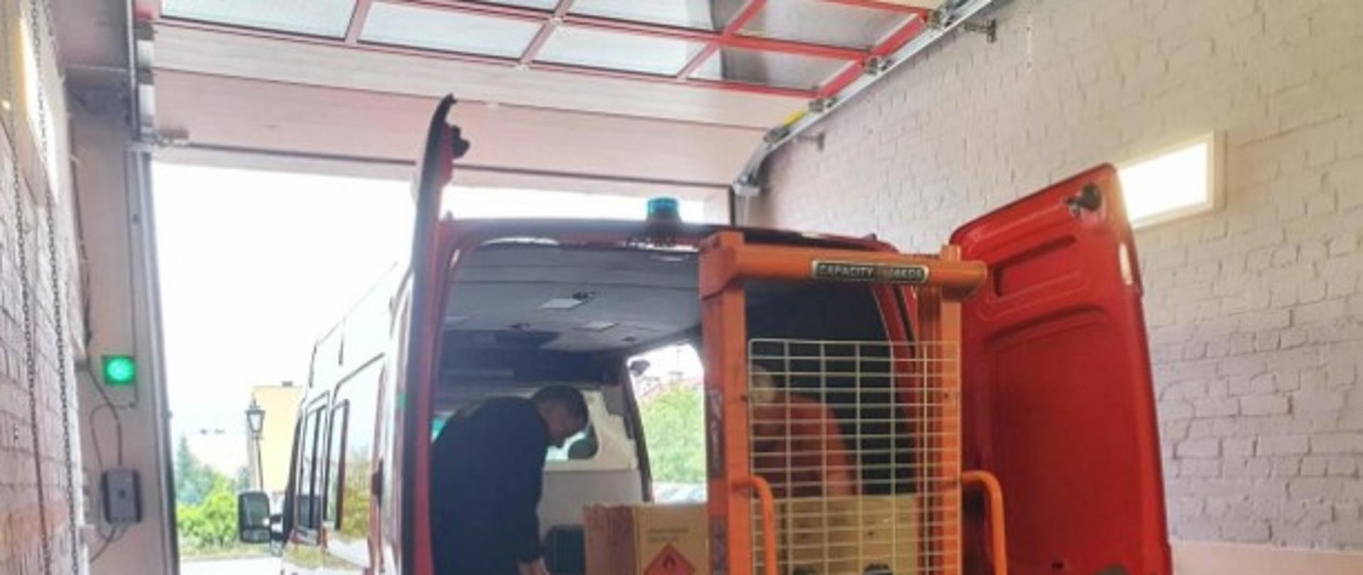 Załadunek środków ochrony indywidualnej na samochód należący do jednej z Ochotniczych Straży Pożarnych pomocą ręcznego wózka paletowego.