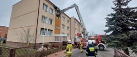 Strażacy przy pomocy podnośnika hydraulicznego usuwają naderwaną część dachu na budynku mieszkalnym wielorodzinnym. 