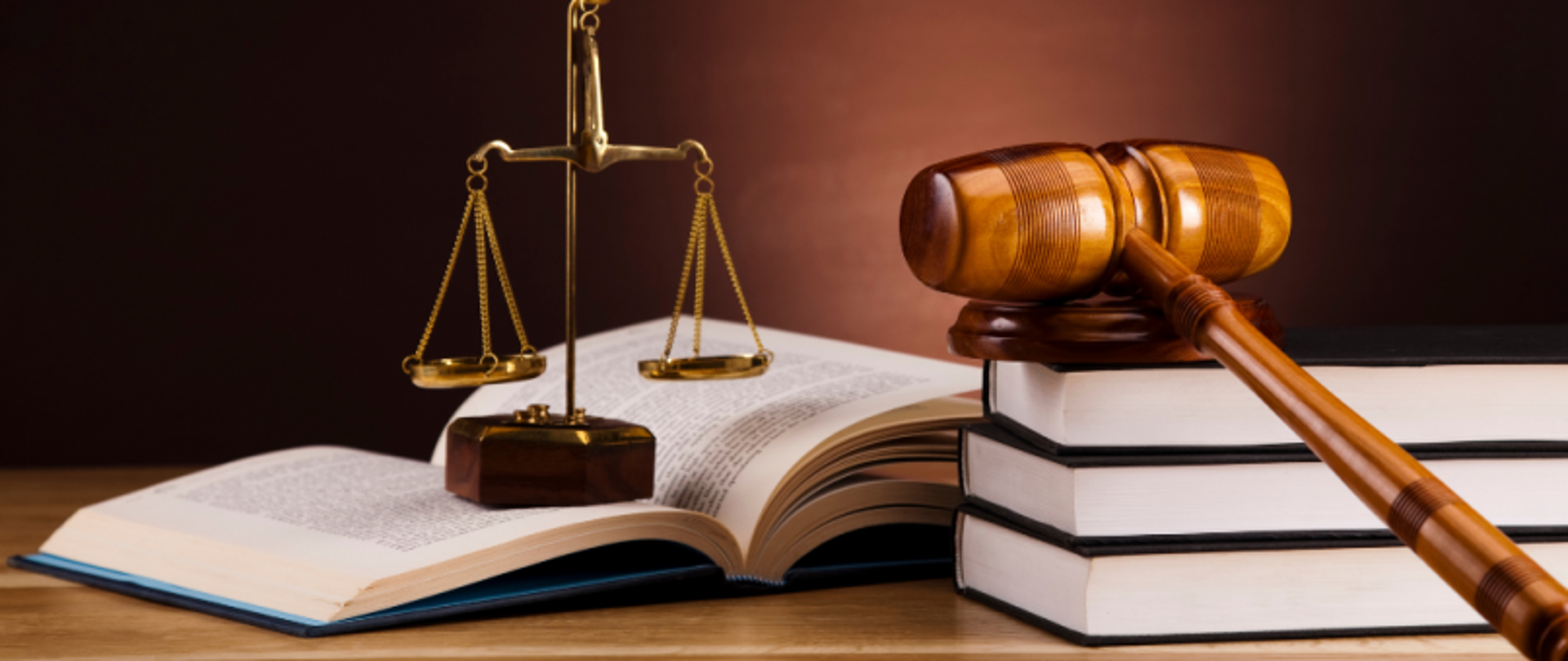 Blat biurka. Na nim leżą książki, młotek sędziowski na podstawce i ozdobna waga.