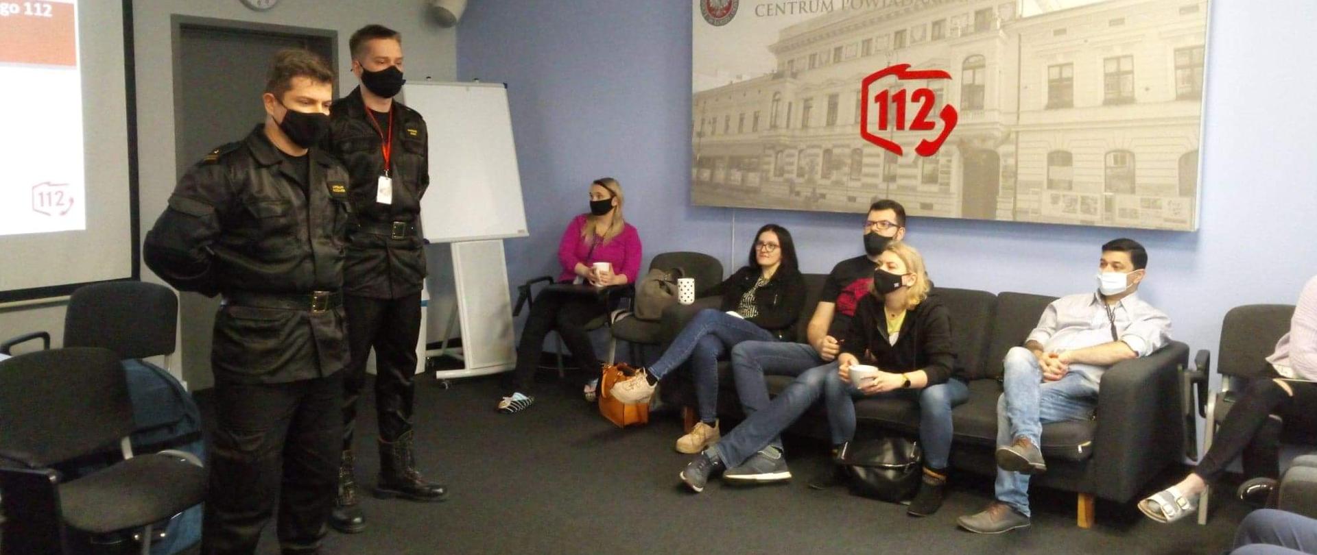 na zdjęciu widać dwóch strażaków prowadzący zajęcia w sali oraz sześć osób cywilnych siedzących w tle tablica