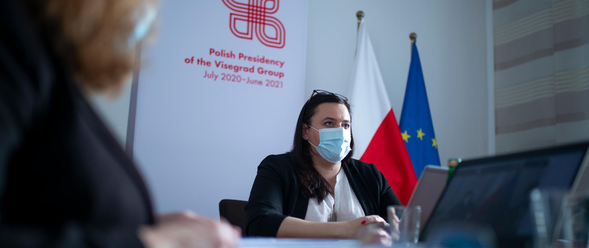 Na zdjęciu siedzi przy stole wiceminister Małgorzata Jarosińska-Jedynak, w tle logo polskiej prezydencji w Grupie Wyszehradzkiej.