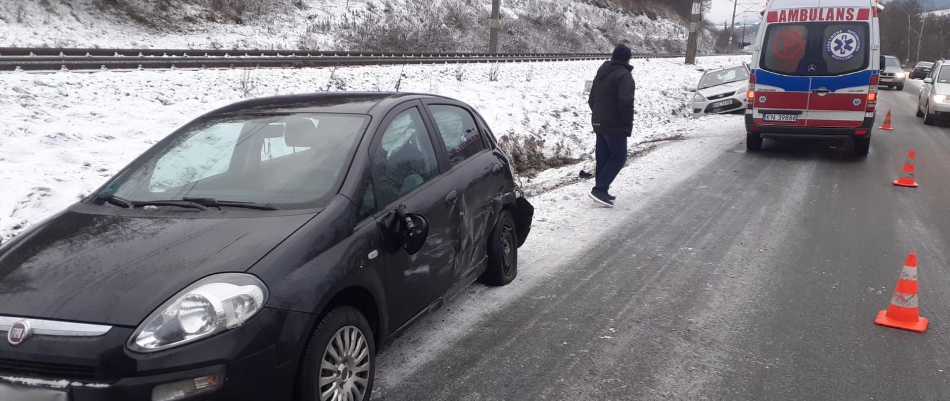 Samochód uczestniczący w zdarzeniu n poboczu. W oddali karetka Pogotowia ratunkowego.