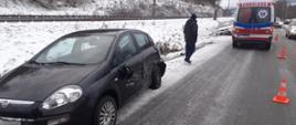 Samochód osobowy na poboczu a w tle karetka Pogotowia ratunkowego.