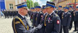 Z-ca komendanta głównego wręcza odznaczenie oficerowi PSP, w tle inni strażacy