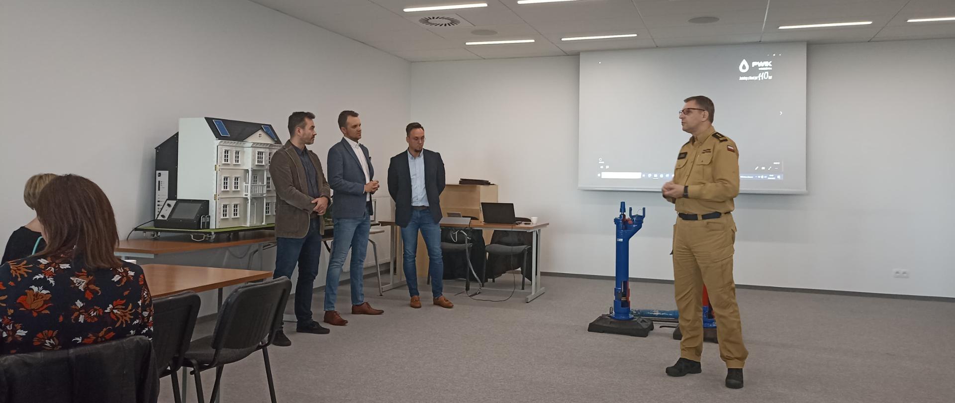 Zdjęcie przedstawia funkcjonariusza PSP i czterech prelegentów w sali narad