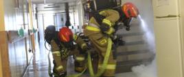 Dwóch strażaków w pochylonej pozycji przeszukuje lokalizują źródło pożaru
