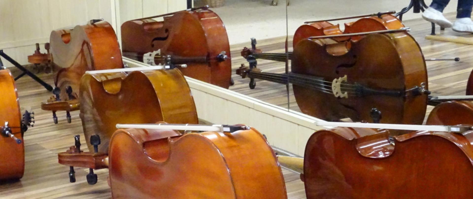 Zdjęcie przedstawia wiolonczele leżące na podłodze w lustrzanym odbiciu