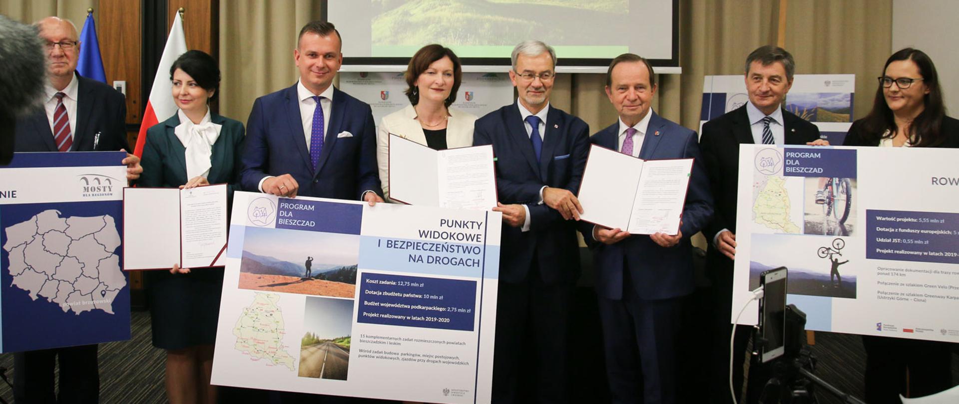 Minister Jerzy Kwieciński wraz z innymi uczestnikami spotkania stoi, a w ręku trzyma podpisane umowy.