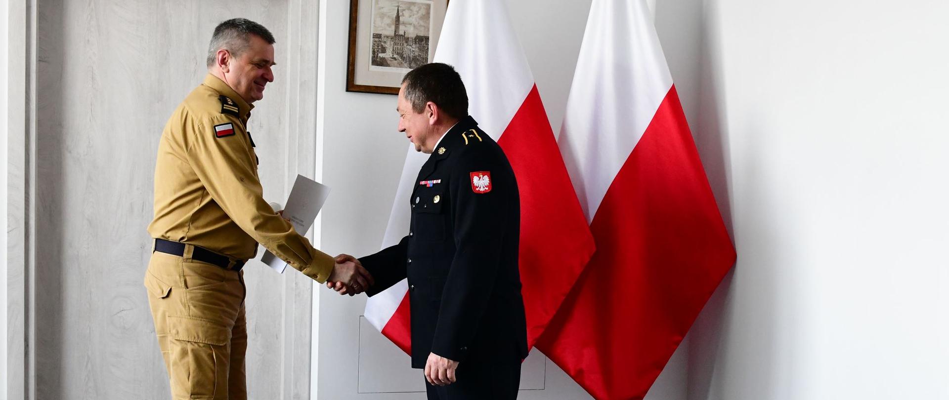 Pomorski komendant wojewódzki Państwowej Straży Pożarnej uściska dłoń strażaka wręczając mu list gratulacyjny.