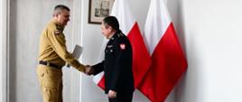 Pomorski komendant wojewódzki Państwowej Straży Pożarnej uściska dłoń strażaka wręczając mu list gratulacyjny.